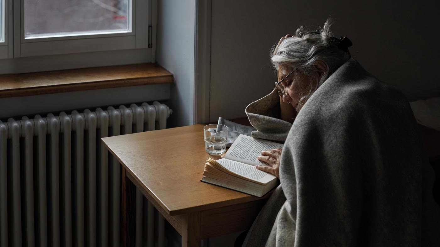 Ältere Frau sitzt am Tisch und liest in einem Buch.